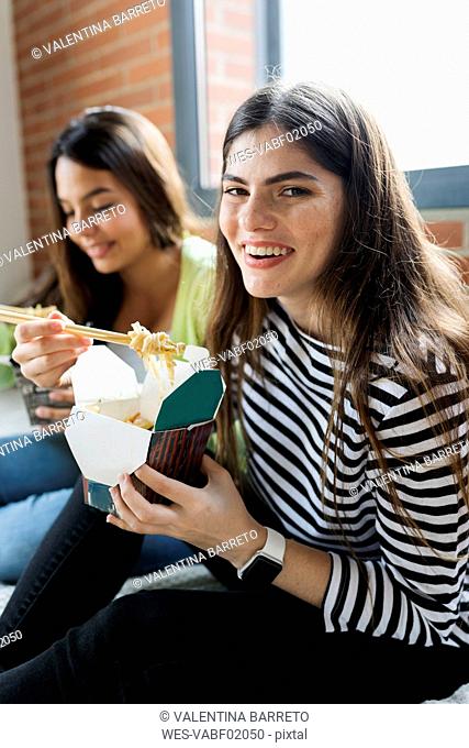 Two happy young women having Asian takeaway food at home