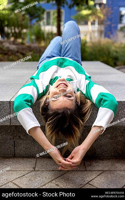 Happy young woman lying on concrete bench