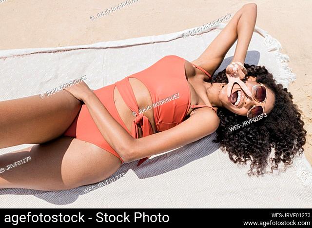 Cheerful woman showing peace sign while sunbathing on sunny day