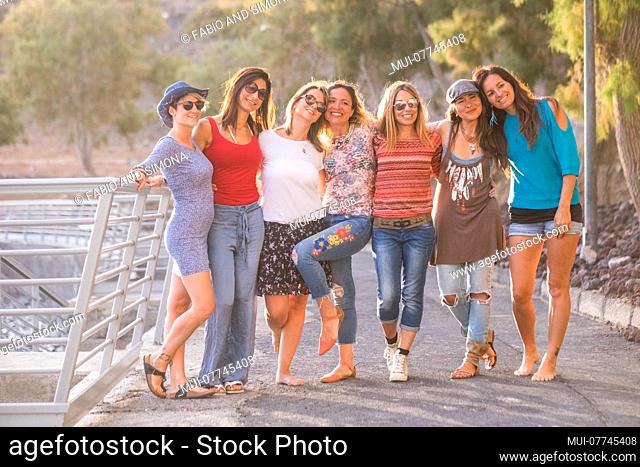 group of seven nice and beautiful caucasian girls young women have fun and laugh and smiles outdoor near the ocean during the sunset