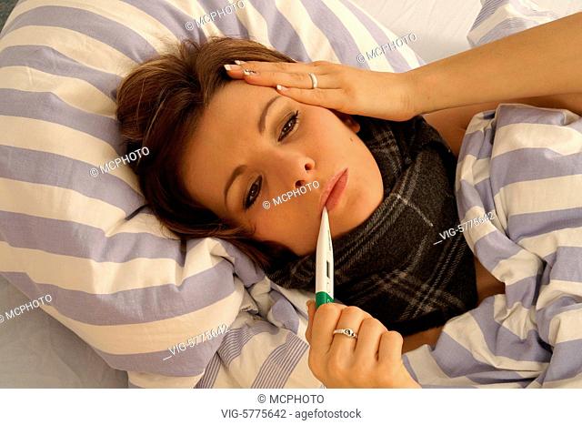 Eine junge Frau liegt mit Fieberthermometer krank im Bett, 2006 - Hamburg, Germany, 26/01/2006