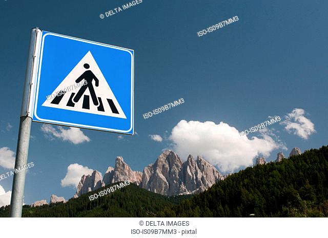 Pedestrian crossing sign over Odle mountains and blue sky, Funes Valley, Dolomites, Italy