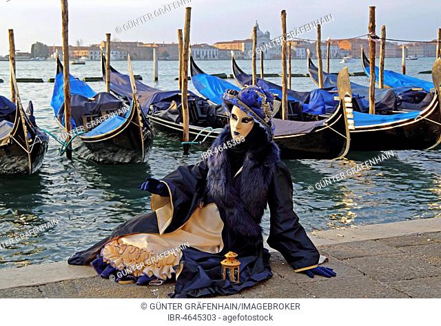 Woman with Venetian mask sitting at the lagoon, behind San Giorgio, carnival in Venice, Venice, Italy