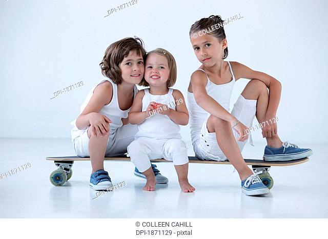 three young girls sitting on a longboard