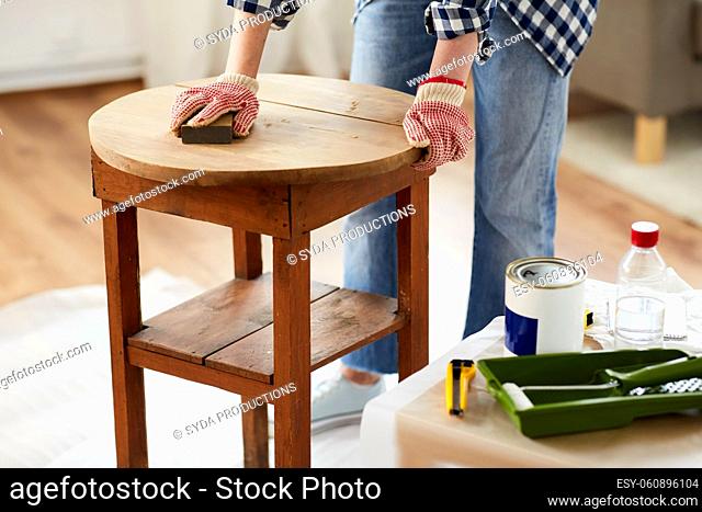 woman sanding old round wooden table with sponge