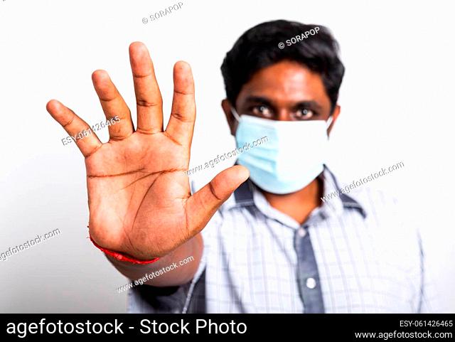 Closeup Asian handsome black man wearing surgical hygienic protective cloth face mask against coronavirus and raising hand stop sign