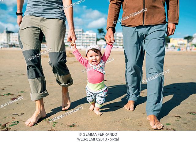 France, La Baule, portrait of happy baby girl walking on the beach with father and grandfather