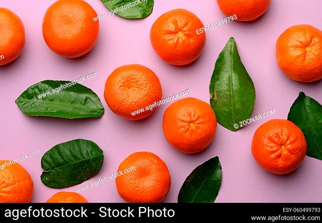 ripe tangerines and green leaves on a purple background, top view