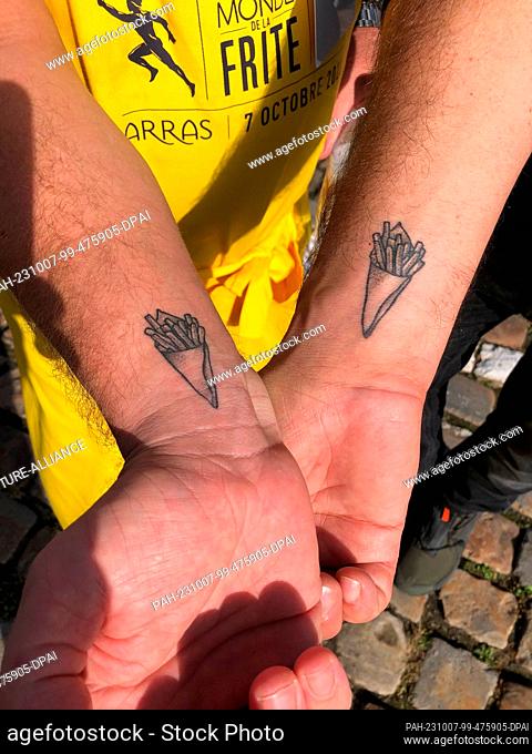 07 October 2023, France, Arras: Belgian restaurateurs Fabian Frances (l) and Sébastian Viloria (r) have a bag of French fries tattooed on their wrists