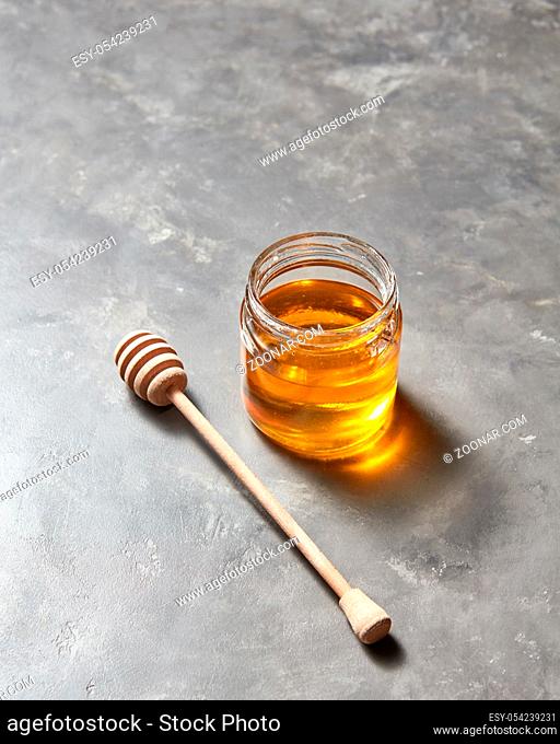Sweet flower natural honey in a jar and wooden spoon on a gray concrete table, place for text . Rosh hashanah jewish New Year holiday concept