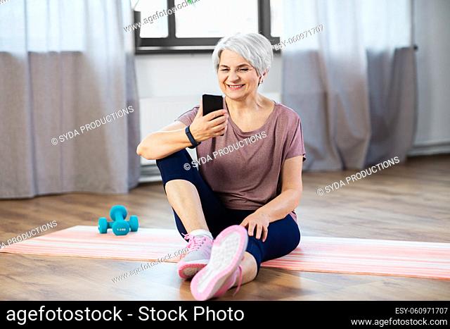 senior woman with smartphone exercising at home