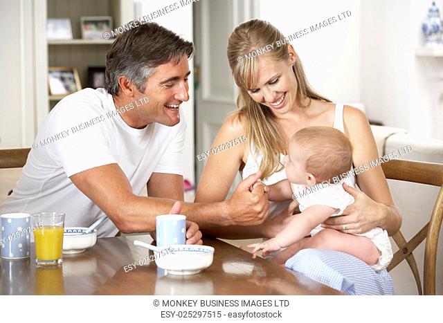 Family With Baby Having Breakfast In Kitchen Together