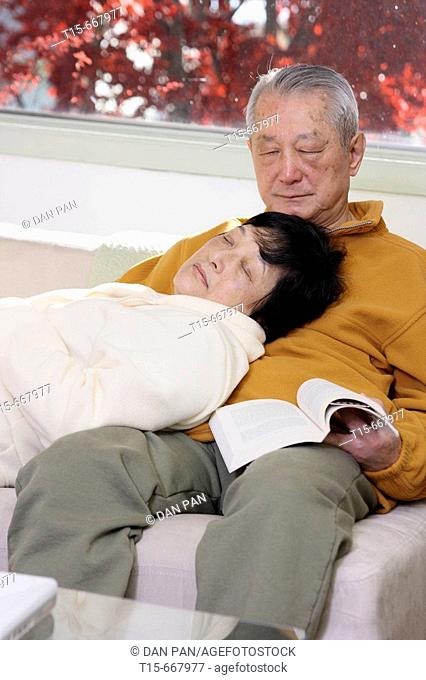 Senior Asian couple falling asleep on sofa while reading