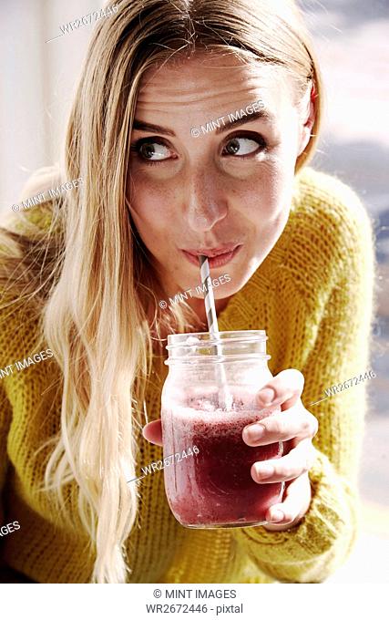A young woman leaning over and sipping a smoothie from a straw