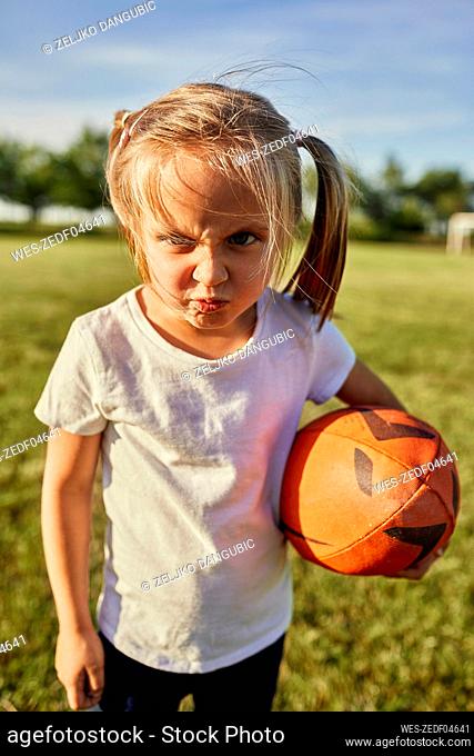 Blond girl with rugby ball making face at sports field on sunny day