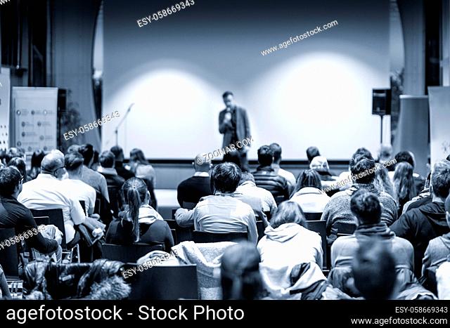 Male public speaker giving a talk at business meeting conference. Rear view of unrecognized people sitting in audience in the conference hall