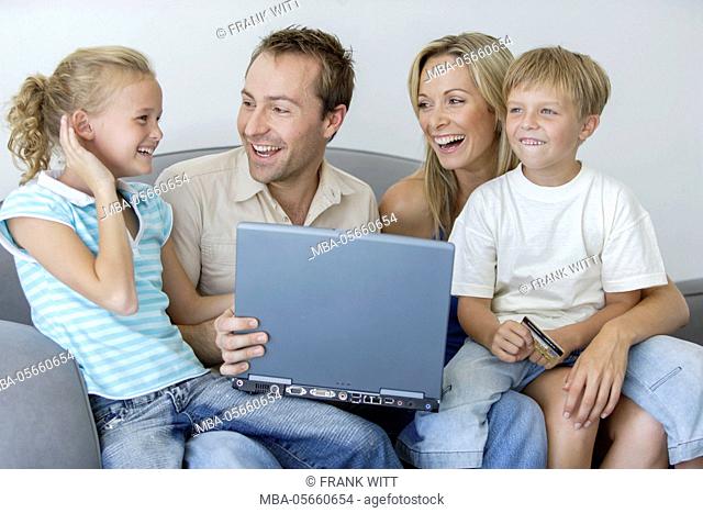 Family with 2 children is sitting with laptop and credit card on sofa