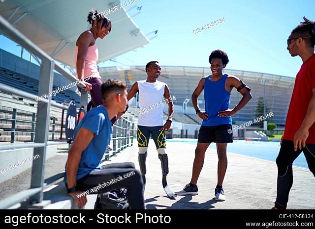 Runner and amputee friends talking on sunny sports track