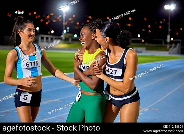 Happy female track and field athletes celebrating and hugging on track