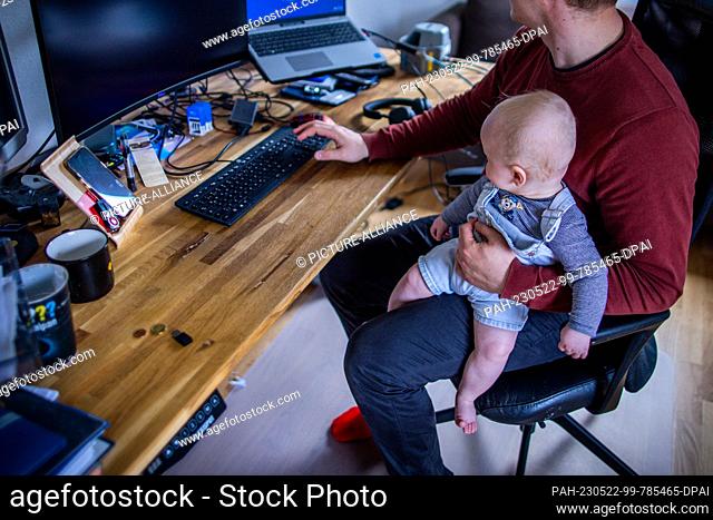 PRODUCTION - 10 May 2023, ---: A young father sits in his home office with his six-month-old son. Photo: Jens Büttner/dpa. - ---/Germany
