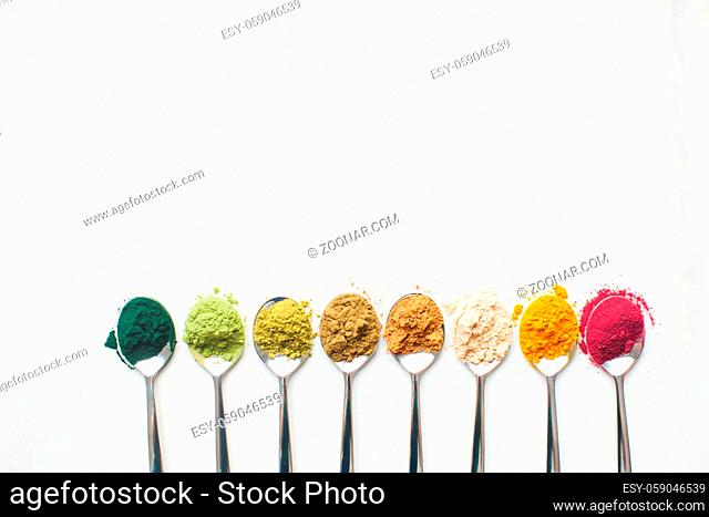 Spoons with different colorful superfood powders withc providing a fortifying effect on white marble table, place for text