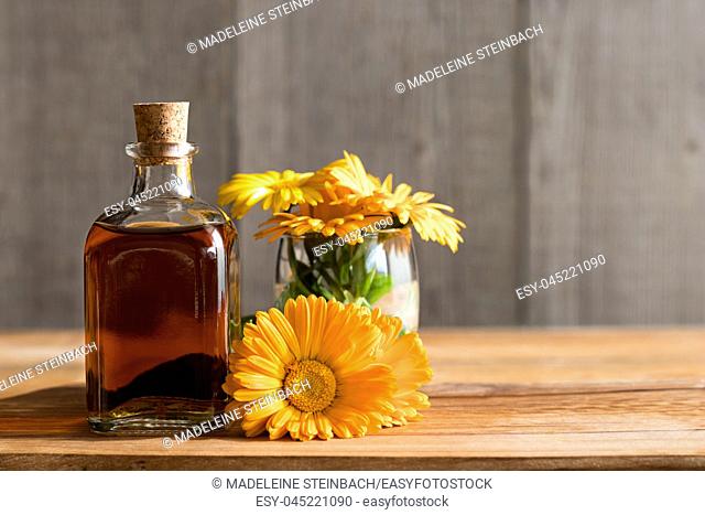 A bottle of calendula (marigold) tincture with fresh calendula flowers on a wooden background