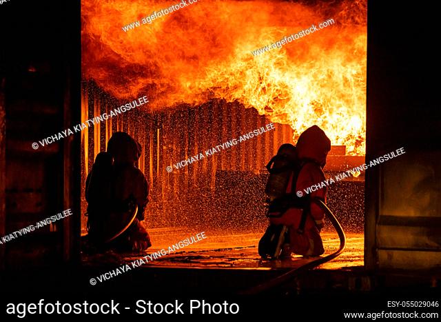 Firefighters using water fog fire extinguisher to fighting with the fire flame in large building. Firefighter and industrial safety disaster and public service...