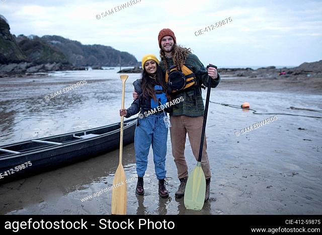 Portrait happy couple with canoe and oars on beach