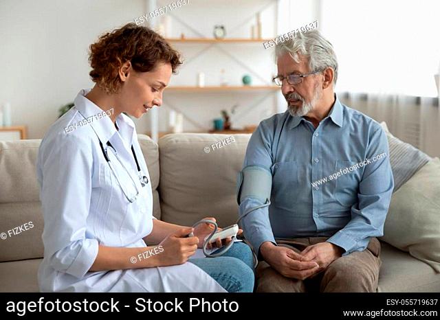 Woman doctor cardiologist or physician checking high blood pressure examining old male patient using tonometer during home medical care visit