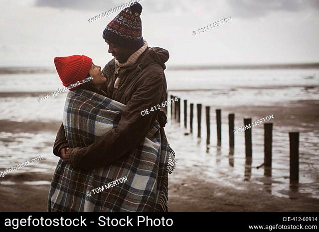 Happy couple wrapped in blanket on winter beach