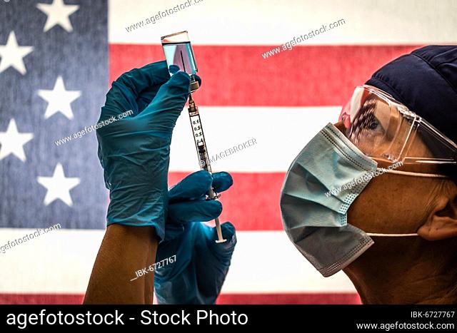 Front line worker holding syringe and vial filled with coronavirus vaccine or medicine silhouetted against american flag