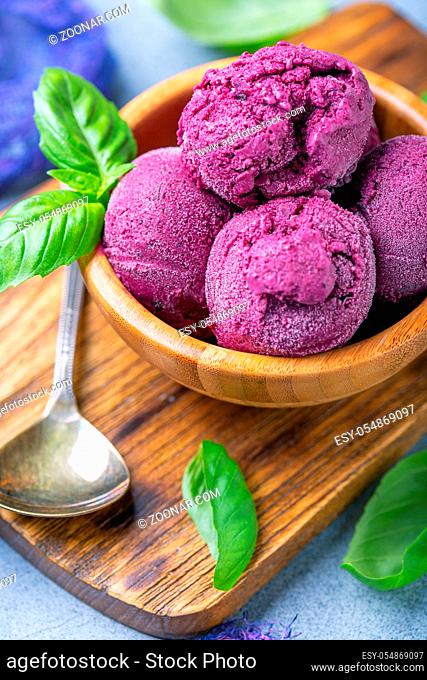 Artisanal ice cream with blueberry and green basil in wooden bowl on serving board, selective focus