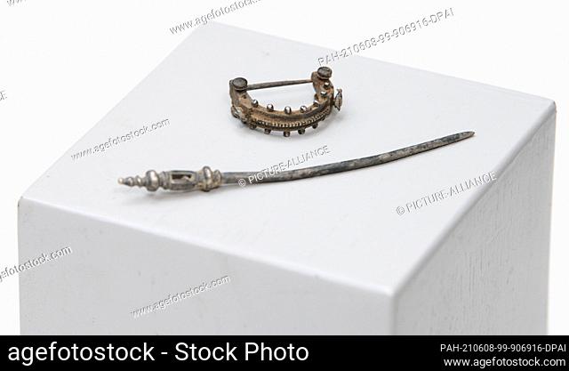 08 June 2021, Bavaria, Augsburg: A fibula (h) and a hairpin lie on a pedestal. These belong to excavation finds from the Roman period which