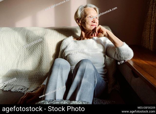 Smiling senior woman with hand on chin sitting at home