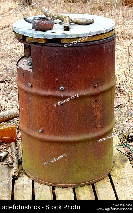 Large rusty barrel is used in the spring forest as a public cigarette ashtray