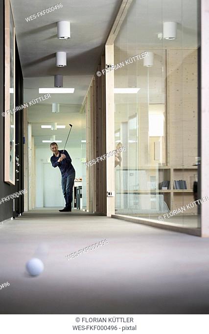 Business man playing golf in corridor of modern office