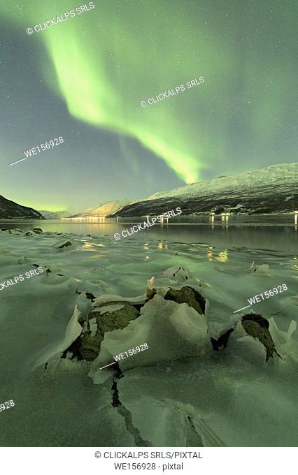 Northern Lights reflected in the cold sea frames the rocks covered with ice Manndalen Kafjord Lyngen Alps Tromsø Norway Europe