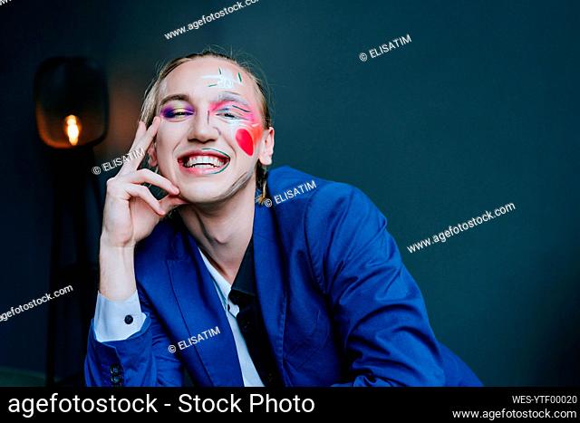 Smiling man with make-up in front of wall