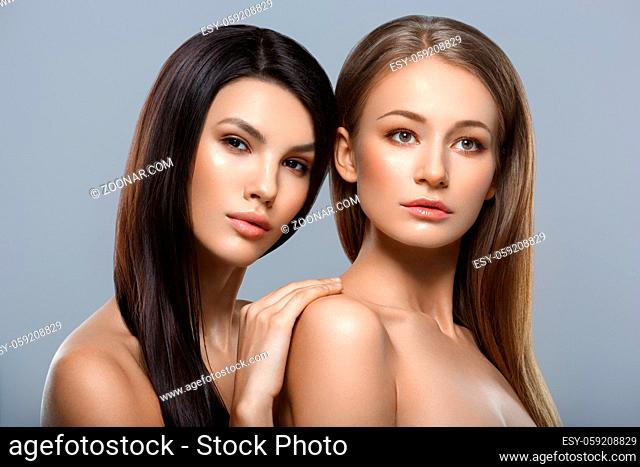 two beautiful young women with natural glowing makeup and long straight hair. beauty shot on gray background. copy space
