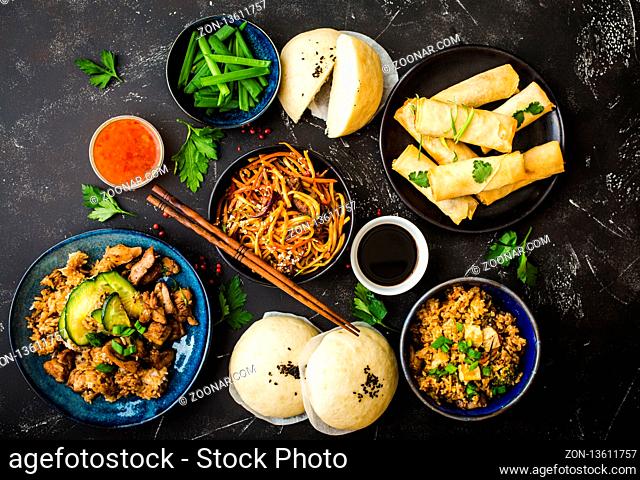 Asian assorted food set, dark rustic stone background. Chinese dishes. Chinese stir-fry noodles, asian rice with meat, dim sum, fried spring rolls