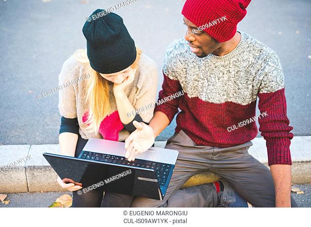 Couple using laptop on pavement