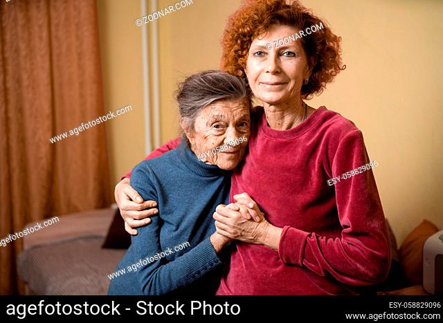 Elderly old cute woman with Alzheimer's very happy and smiling when eldest daughter hugs and takes care of her, at home on sofa