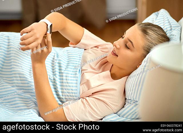 smiling girl with smart watch lying in bed at home