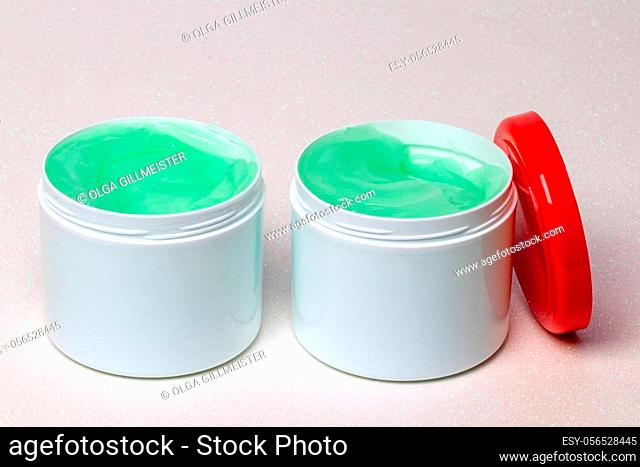 Closeup oft two opened plastic jar or container with green cooling gel (horse balm) for sports injuries or Aloe vera cosmetic gel on a bright background