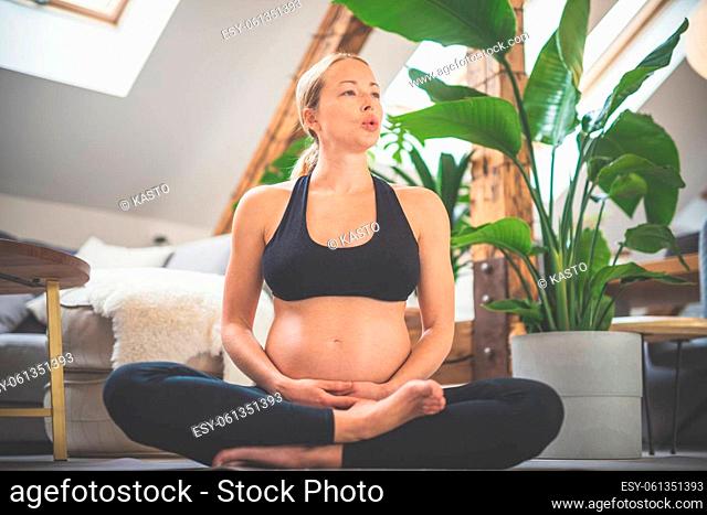 Young beautiful pregnant woman training yoga, caressing her belly. Young happy expectant relaxing, thinking about her baby and enjoying her future life