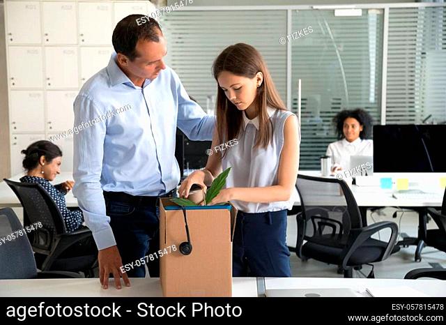 Colleague businessman supporting dismissal upset woman pack belongings in cardboard box, preparing to leave office, sad female office worker despair