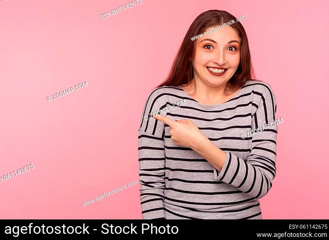 Look, awesome advertise. Portrait of cheerful pretty woman in striped sweatshirt pointing aside and smiling, laughing at something funny on copy space