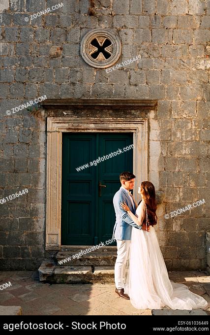 The bride and groom are embracing at the wooden green door of an ancient building in Perast. High quality photo