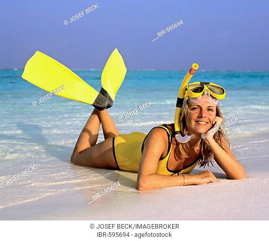 Young woman laying on beach with snorkeling gear, Maldives, Indian Ocean
