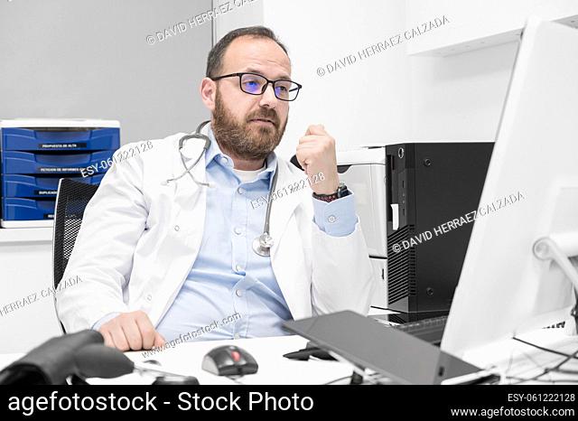 Portrait of friendly smiling healthcare professional therapist sitting at workplace. Happy confident male doctor physician wearing white medical coat and...
